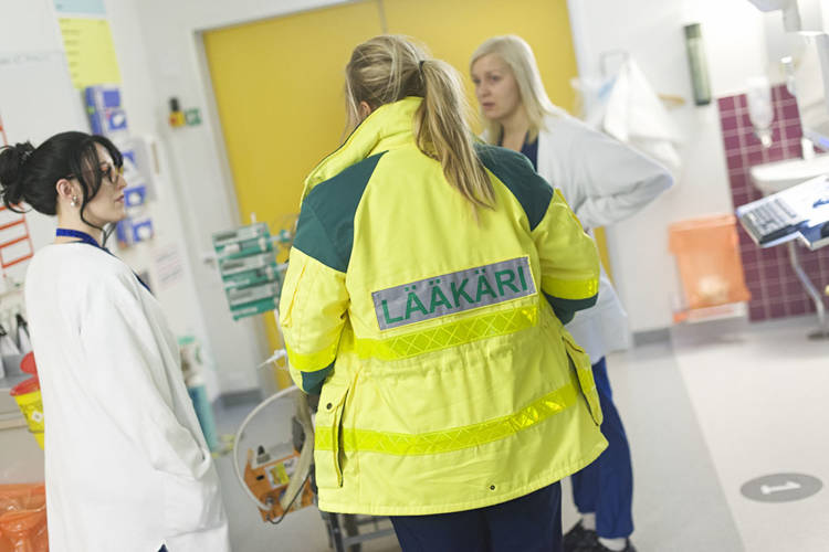 På sjukhusets korridor finns jourläkaren och två sjuksköterskor. Läkaren har på sig en gul reflexväst med texten "Lääkäri" på ryggen.