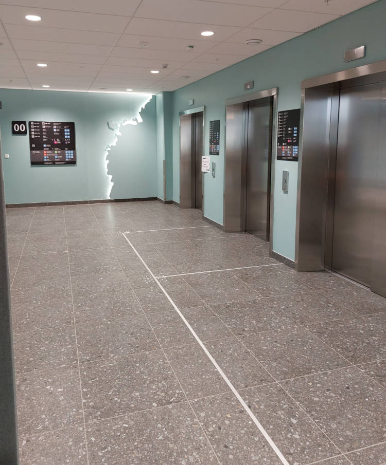 Kuvassa näkyy kolme hissiä vierekkäin käytävän päässä.