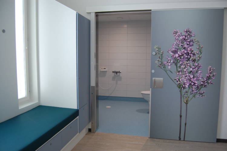 Potilashuoneen suihku- ja wc-tilan liukuovessa on kaunis violettisävyinen kuva kukasta.