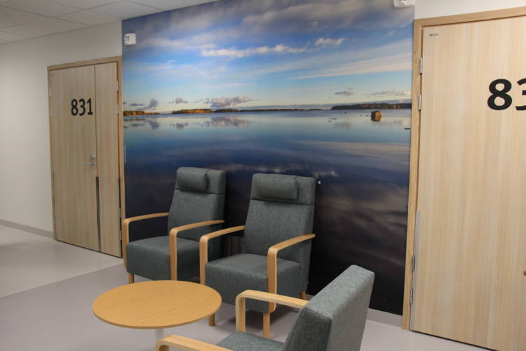 Bilden visar tre fåtöljer och ett lågt runt bord, på väggen finns en fototapet av ett hav och skärgård. Vattnets yta är lugn och moln reflekteras på den.