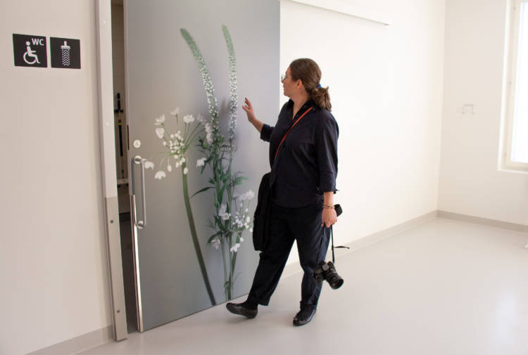 Sandra Kantanen betraktar ett bildtryck som består av en förstoring av en blomma på en grå skjutdörr. Blommorna är vita och skaften gröna. 