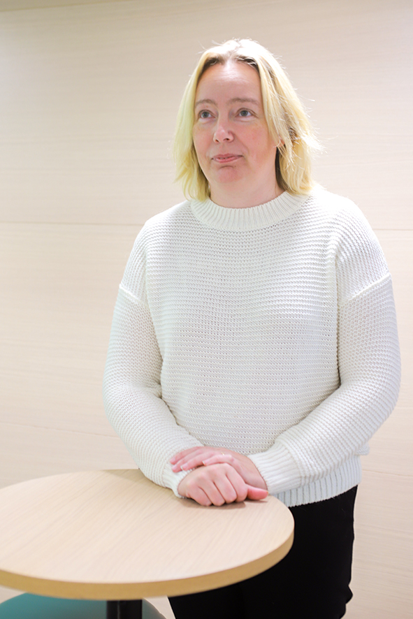 Osastonhoitaja Marlene Vägar seisoo pöydän ääressä. Hänellä on vaaleat hiukset, valkoinen paita ja mustat housut.  
