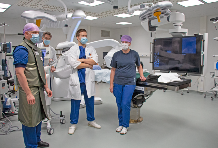 Tre läkare och en operationssköterska står på operationssalen. Personen längst till vänster bär strålskyddsutrustning.