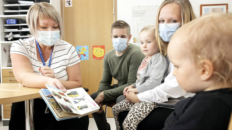 Terveydenhoitaja Ulrika Bärnas istuu työpisteellään kirjoituspöydän ääressä. ja näyttää perheelle jotain kirjasta.