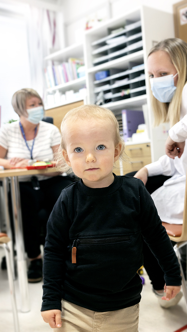 2-vuotias Melvin-poika kävelee vastaanottohuoneessa. Taustalla näkyvät terveydenhoitaja Ulrika Bärnas sekä Melvinin vanhemmat.