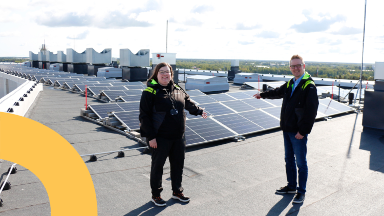 Jenni Siirilä ja Toni Ahola seisivat H-talon katolla ja osoittavat takana olevia aurinkopaneeleja.