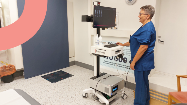 Sairaanhoitaja seisoo valokuvauslaitteen äärellä ja katsoo näyttöruutua.