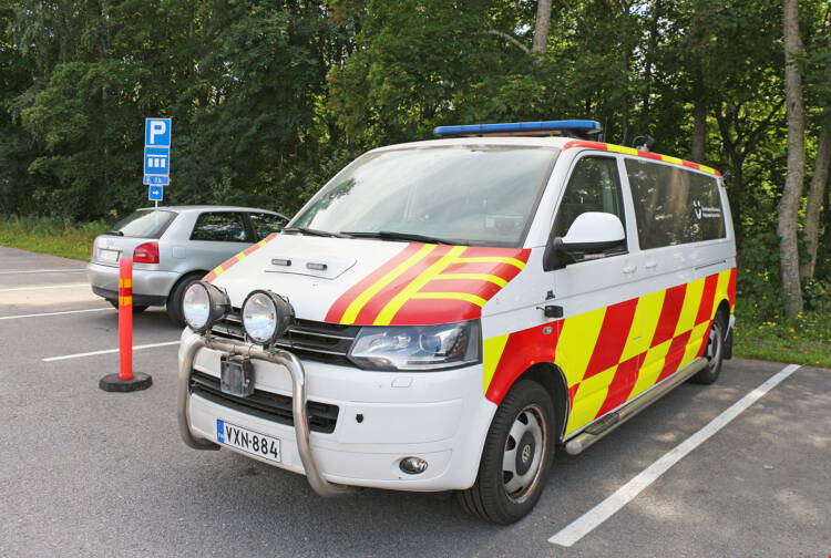 Ambulanssin näköinen valkoinen pakettiauto, jossa on puna-keltaiset teippaukset ja sininen valo katolla.