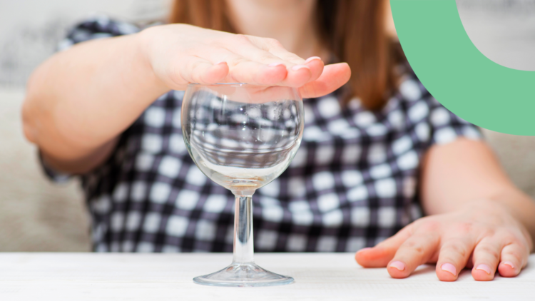 A women is sitting at the table. She has an empty wine glass in front of her and is holding her hand on top of the glass as a sign of not letting anyone fill the glass with alcohol.