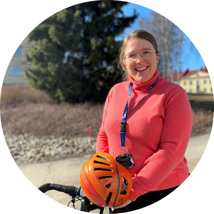 En leende Petra Fager lutar sig mot en cykel. Hon håller en orange cykelhjälm i handen.